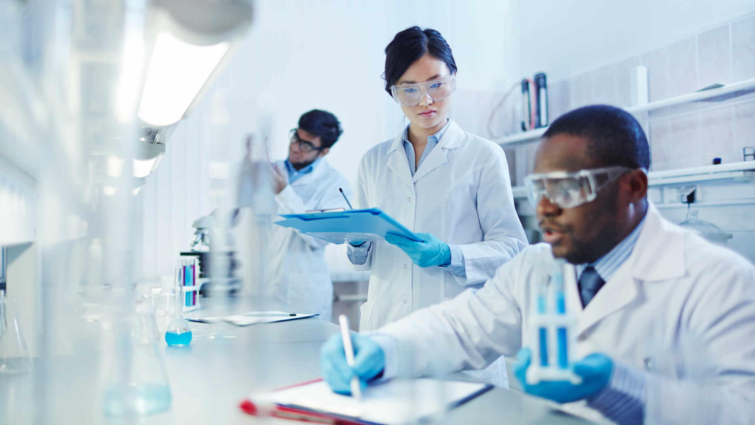 A lab technician taking notes while her partner runs a test